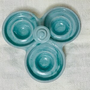 May include: A light blue ceramic egg holder with three individual compartments. The holder has a swirl design and is perfect for holding eggs.