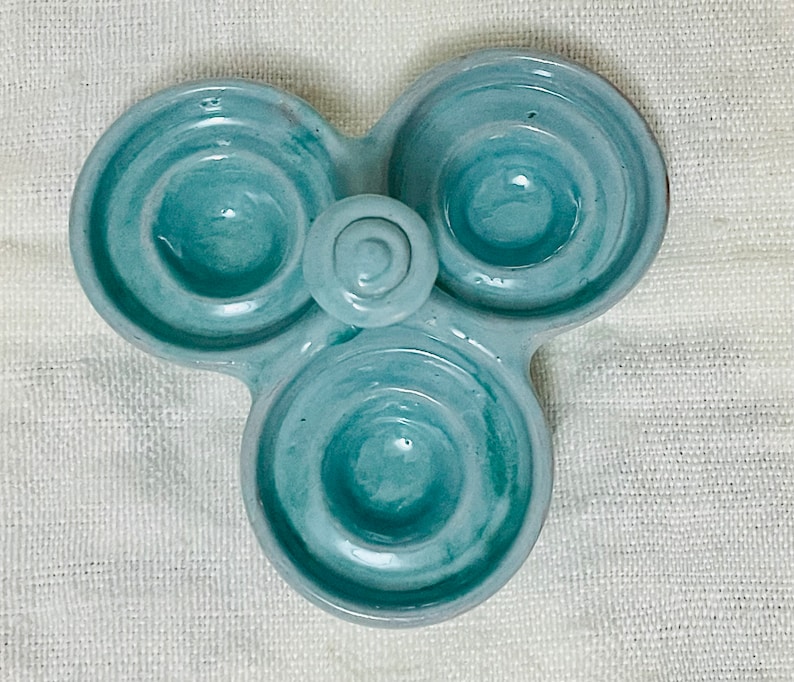 May include: A light blue ceramic egg holder with three individual compartments. The holder has a swirl design and is perfect for holding eggs.
