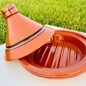 May include: A terracotta tagine with a domed lid. The tagine has a black rim and a black stripe around the middle. The lid has two black stripes around the middle.