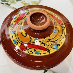 May include: A brown ceramic serving dish with a lid. The dish is decorated with a colorful floral pattern in shades of yellow, orange, red, blue, and white.