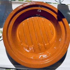 May include: A terracotta round dish with a raised, ridged center. The dish is glazed and has a shiny finish.