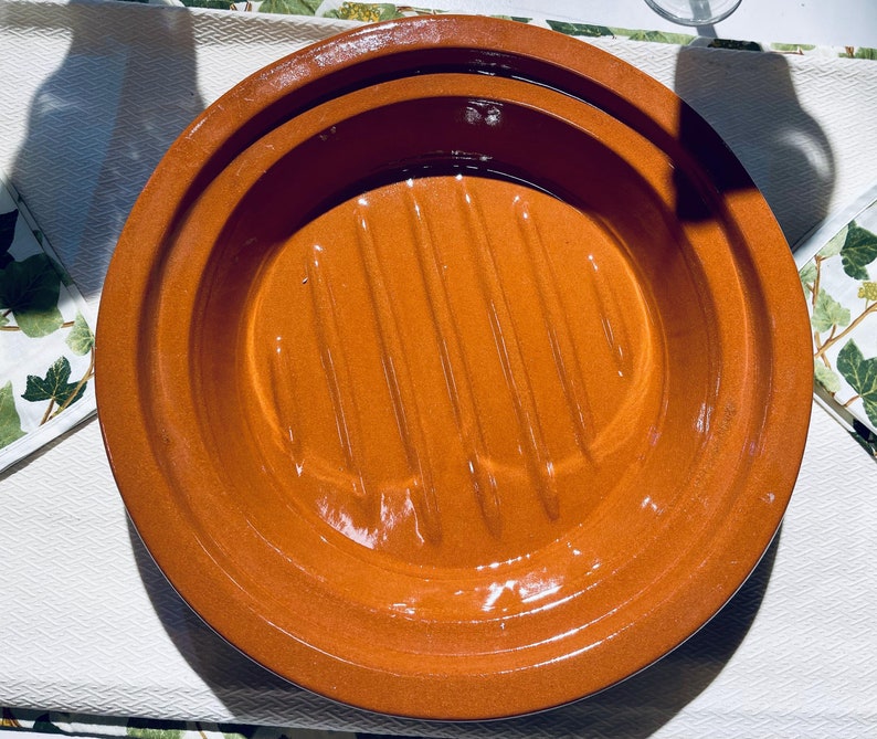 May include: A terracotta round dish with a raised, ridged center. The dish is glazed and has a shiny finish.