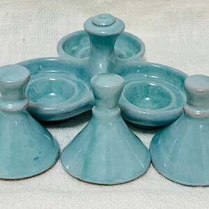 May include: A set of five light blue ceramic egg cups. The cups are shaped like small bowls with a raised centre. The set includes a central piece with three smaller cups attached.