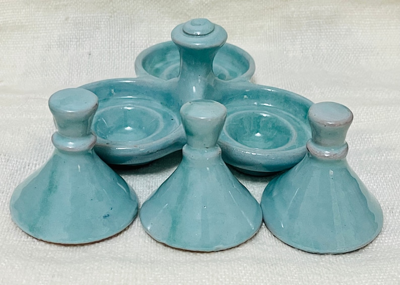 May include: A set of five light blue ceramic egg cups. The cups are shaped like small bowls with a raised centre. The set includes a central piece with three smaller cups attached.