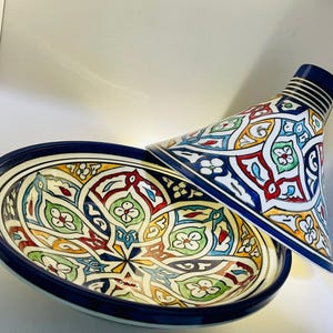 May include: A colorful ceramic tagine with a blue rim and intricate geometric patterns in shades of red, green, yellow, and blue.