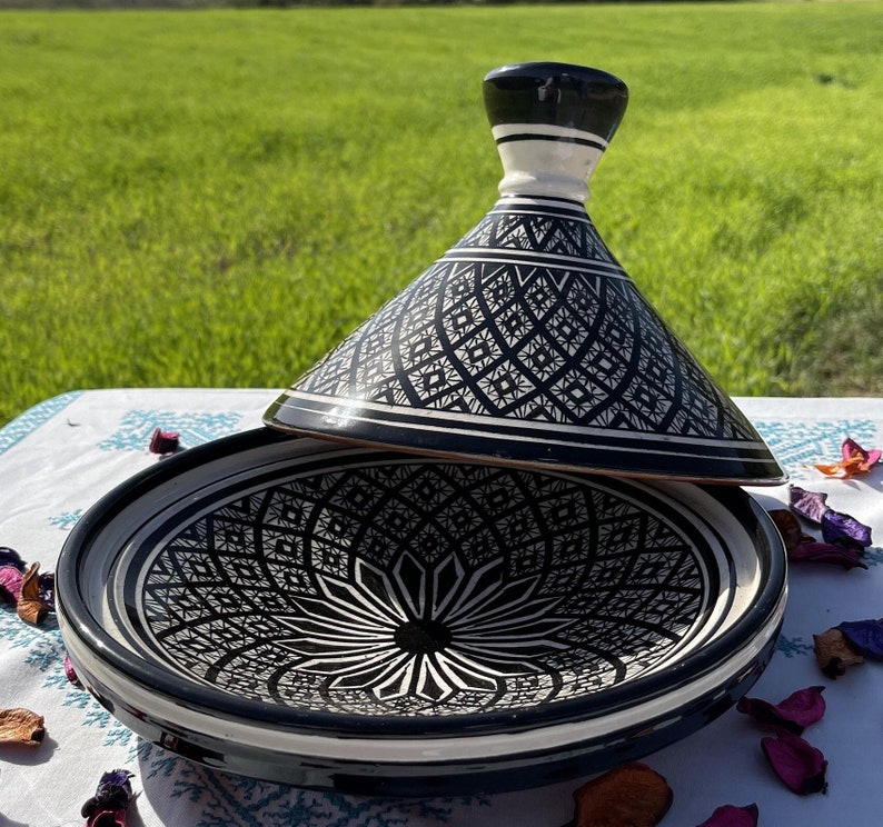 Może przedstawiać: Czarno-biała ceramiczna tagine z misternymi geometrycznymi wzorami. Pokrywka jest lekko uchylona, odsłaniając wnętrze naczynia.