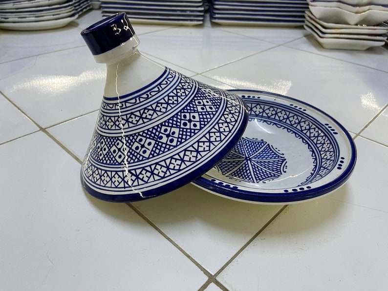 May include: A white ceramic tagine with a blue and white geometric pattern. The tagine is open and the lid is resting on the side of the dish.