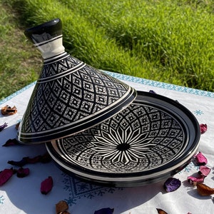 Może przedstawiać: Czarno-biała ceramiczna tagine z misternymi geometrycznymi wzorami. Pokrywa jest lekko uchylona, odsłaniając pasujący wz&oacute;r na podstawie.