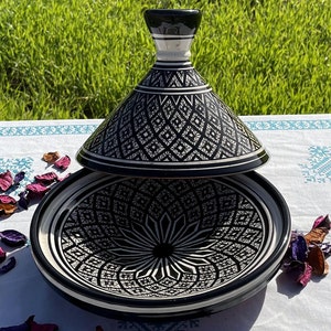 Może przedstawiać: Czarno-biała ceramiczna tagine z geometrycznym wzorem. Pokrywa jest uniesiona, a tagine stoi na białym obrusie.