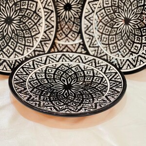 May include: Set of four black and white ceramic plates with intricate geometric designs. The plates feature a central starburst pattern surrounded by concentric rings of geometric shapes.