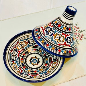 Könnte beinhalten: Eine traditionelle marokkanische Tajine mit einem blauen und weißen Keramikboden und einem passenden Deckel mit komplizierten geometrischen Mustern in Blautönen, Rot, Gelb und Weiß.