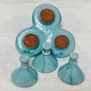 May include: A set of three teal blue ceramic condiment dishes with brown lids. The dishes are shaped like a clover leaf and have three individual compartments. The lids are round and have a smooth, glossy finish.