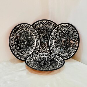 May include: Set of four black and white ceramic plates with intricate geometric designs. The plates are stacked on top of each other.