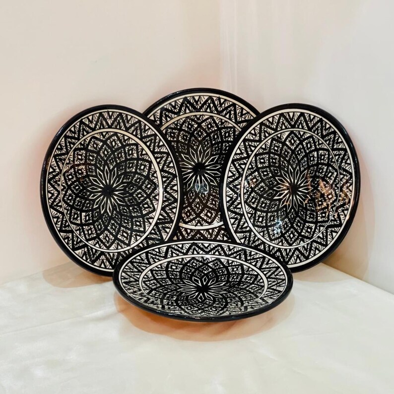 May include: Set of four black and white ceramic plates with intricate geometric designs. The plates are stacked on top of each other.