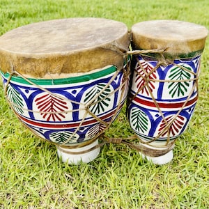 May include: Two ceramic drums with a blue, green, red and white geometric pattern. The drums are tied together with brown string.