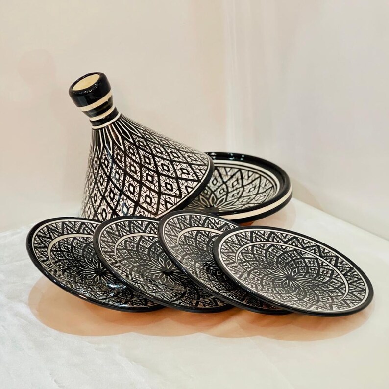 May include: A set of black and white ceramic Moroccan tagine dishes with intricate geometric patterns. The set includes a large tagine with a lid and four smaller plates.