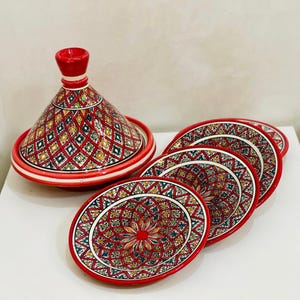 May include: A set of five red ceramic plates with intricate geometric patterns in shades of green, yellow, and white. The plates are arranged in a stack, with the largest plate at the bottom and the smallest plate at the top. A red ceramic tagine pot with a similar geometric pattern is in the background.