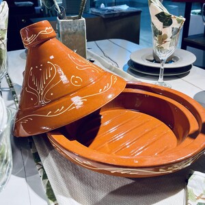 May include: A terracotta tagine with a white glaze and intricate designs. The lid is slightly ajar, revealing the interior of the pot.