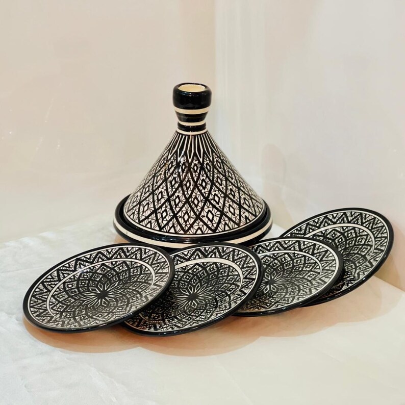 May include: A black and white ceramic tagine with a conical lid and four matching plates. The tagine and plates feature intricate geometric designs.