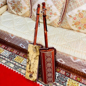 May include: Two traditional Moroccan musical instruments, called the gimbri, with intricate wood carvings and decorative details. The instruments are made of wood and have a long neck and a round body.