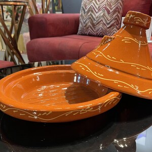May include: A terracotta tagine with a lid, both decorated with a white geometric pattern. The tagine is a traditional Moroccan cooking pot.