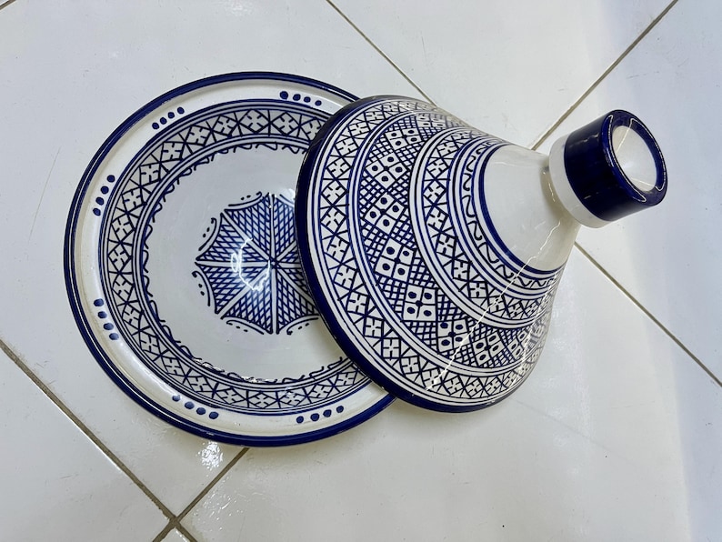 May include: A white ceramic serving dish with a blue and white geometric pattern. The dish has a lid with a knob on top.
