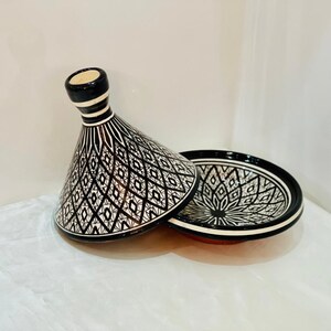 May include: A black and white ceramic tagine with a geometric pattern. The lid is cone-shaped and the base is round.