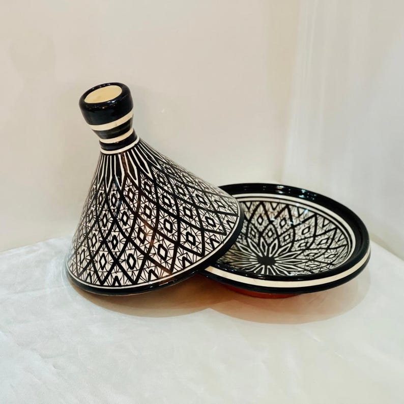 May include: A black and white ceramic tagine with a geometric pattern. The lid is cone-shaped and the base is round.