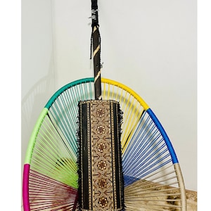 Puede incluir: Un instrumento musical tradicional africano llamado kora, con un cuerpo de madera y diseños intrincados incrustados. La kora está apoyada en una silla arcoíris colorida.