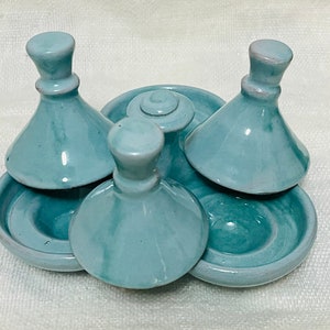 May include: A set of four teal ceramic condiment dishes with lids. The dishes are arranged in a circle with the lids placed on top of the dishes.
