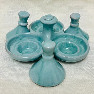 May include: A light blue ceramic egg holder with five individual compartments. The holder has a central pedestal with a rounded top and four smaller pedestals around it.