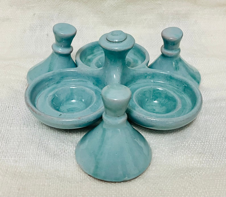May include: A light blue ceramic egg holder with five individual compartments. The holder has a central pedestal with a rounded top and four smaller pedestals around it.