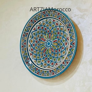 May include: A blue and white ceramic plate with a colorful geometric design. The plate features a central starburst pattern with red, yellow, green, and blue accents. The plate is surrounded by a border of blue and white geometric shapes.