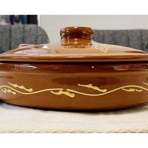 May include: A brown ceramic casserole dish with a lid. The dish has a decorative design of yellow wavy lines around the rim.