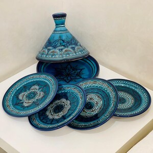 Puede incluir: Un juego de cinco platos de cerámica azul y blanco con intrincados diseños geométricos. Los platos están apilados uno encima del otro, con una tapa de cerámica azul y blanco a juego en la parte superior de la pila. La tapa tiene forma cónica y está decorada con un diseño geométrico similar.