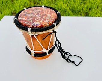 May include: A small wooden drum with a brown and white marbled top, black rope accents, and a black rope handle.