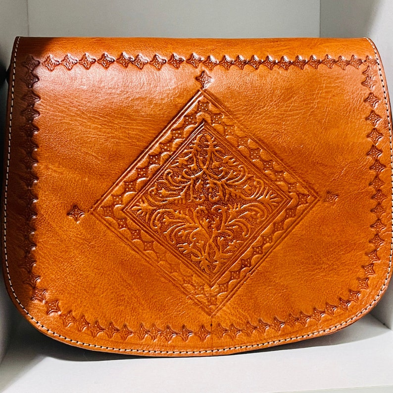 May include: A brown leather satchel bag with a diamond-shaped embossed design. The bag has a flap closure and a stitched border.