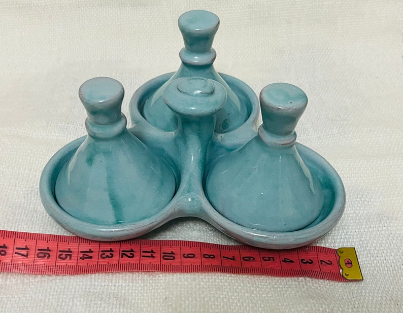 May include: A set of three light blue ceramic condiment dishes with lids. The dishes are arranged in a circle and have a raised centre piece.