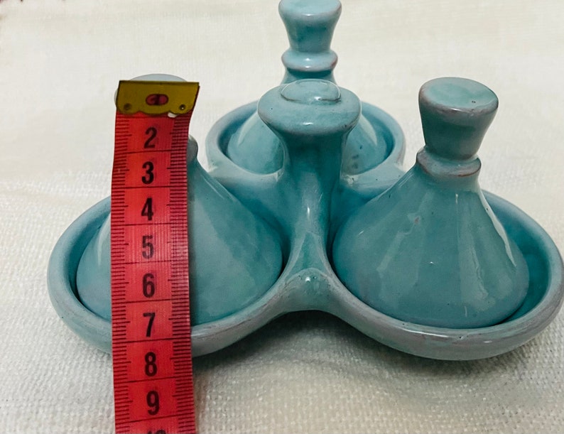 May include: A set of three blue ceramic cruets with a matching blue ceramic base. The cruets have a rounded, bulbous shape with a small spout at the top. The base has three indentations to hold the cruets.