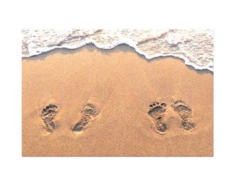 May include: Footprints in the sand near the ocean's edge. The image shows two sets of footprints, one pair close together and another pair further apart, with the foamy white water of the ocean in the background.