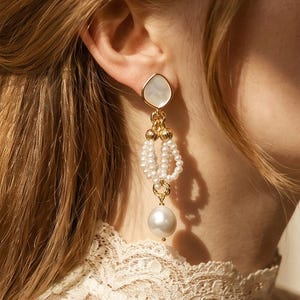 May include: A gold-toned drop earring featuring a teardrop-shaped white stone stud, a central section composed of multiple small white seed pearl loops connected by gold rings, and a single large round white pearl dangling at the very bottom.