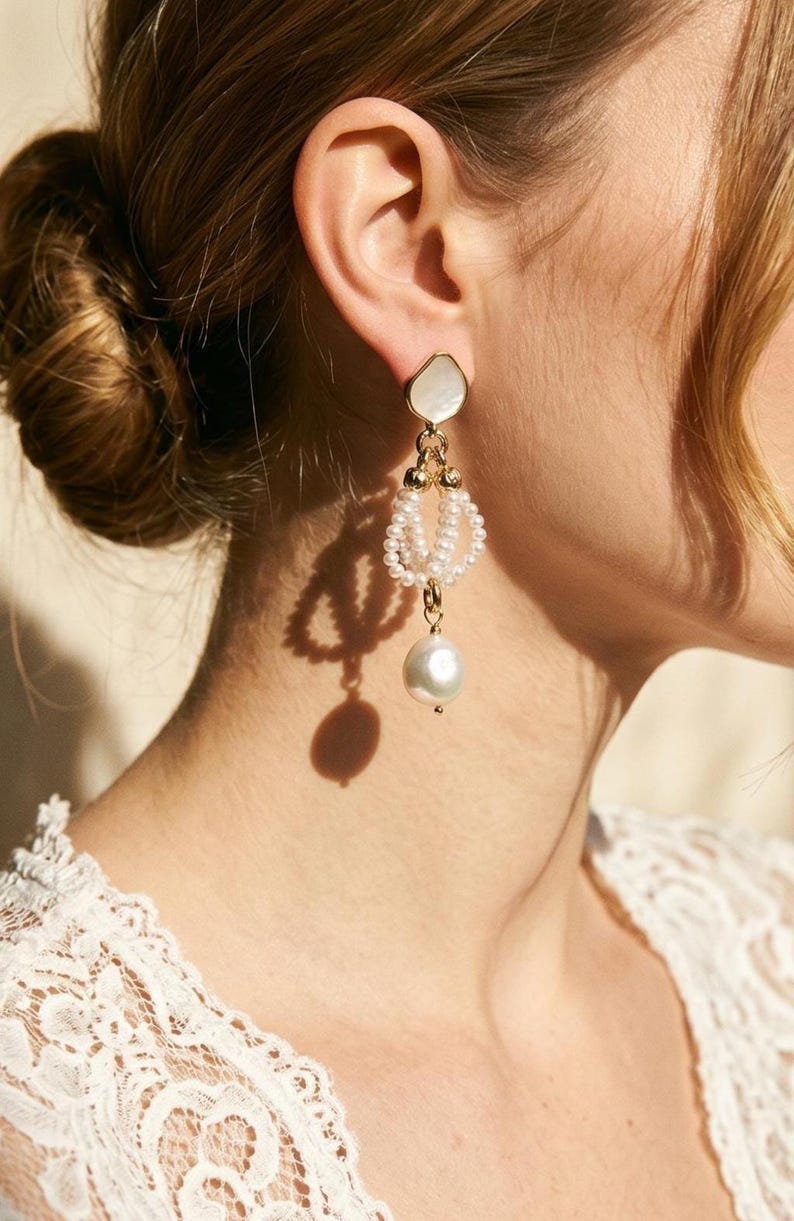 May include: Elegant gold-toned earrings with a pearlescent, irregular-shaped top, a beaded middle section, and a large, dangling pearl. The earrings are designed with a delicate, feminine aesthetic, suitable for special occasions.