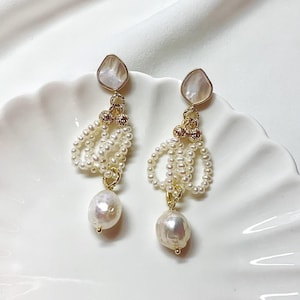 May include: A pair of drop earrings featuring a teardrop-shaped mother-of-pearl stud, gold-toned metal accents, loops of small white seed pearls, and a single larger irregular white baroque pearl dangling at the bottom of each earring.