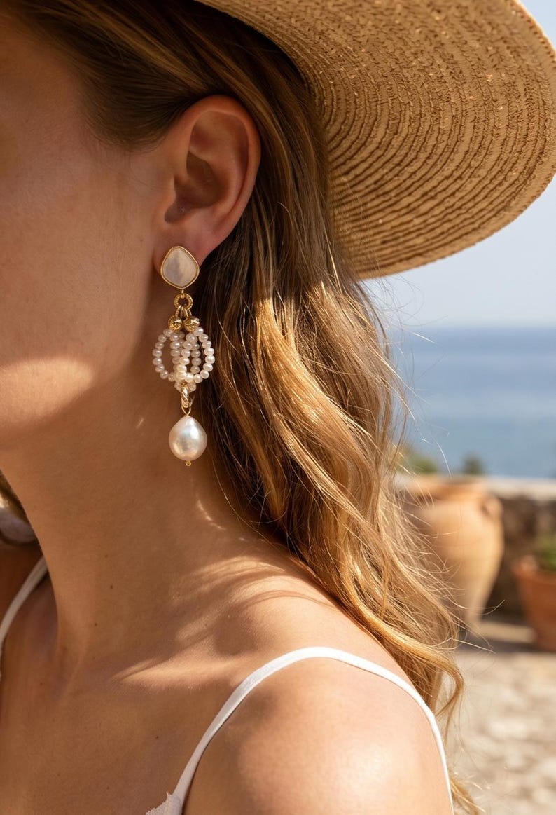 May include: A gold-toned dangle earring featuring a teardrop-shaped mother-of-pearl stud, a central circular cluster of small white seed pearls, and a single large, irregular white baroque pearl drop suspended at the bottom of the earring structure.