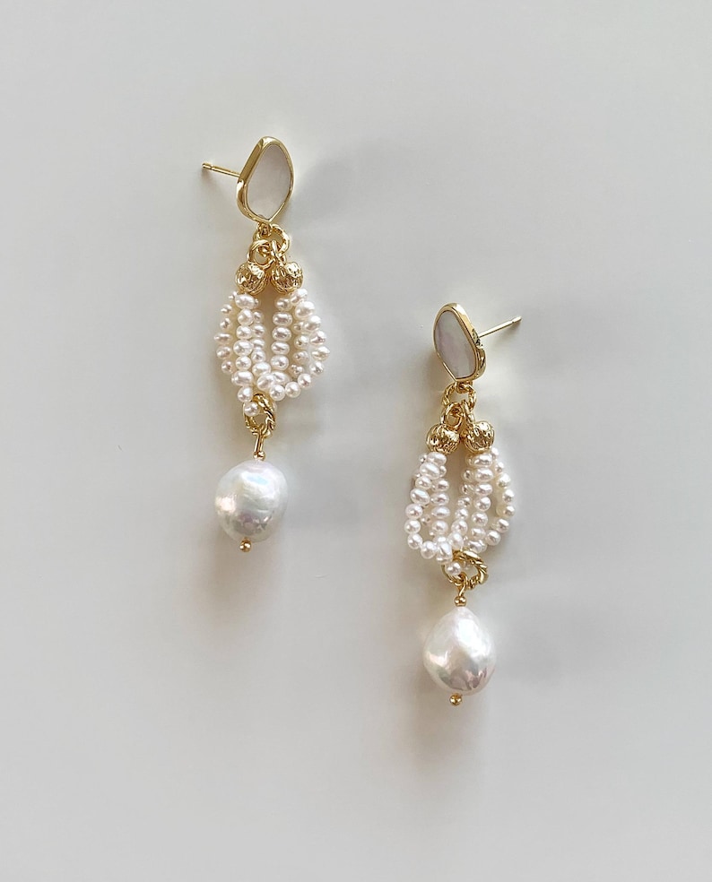 May include: A pair of gold-tone drop earrings featuring a white stone stud, a cluster of small white seed pearls arranged in a loop, and a single larger white baroque pearl dangling at the bottom, all connected by gold-tone metal hardware.
