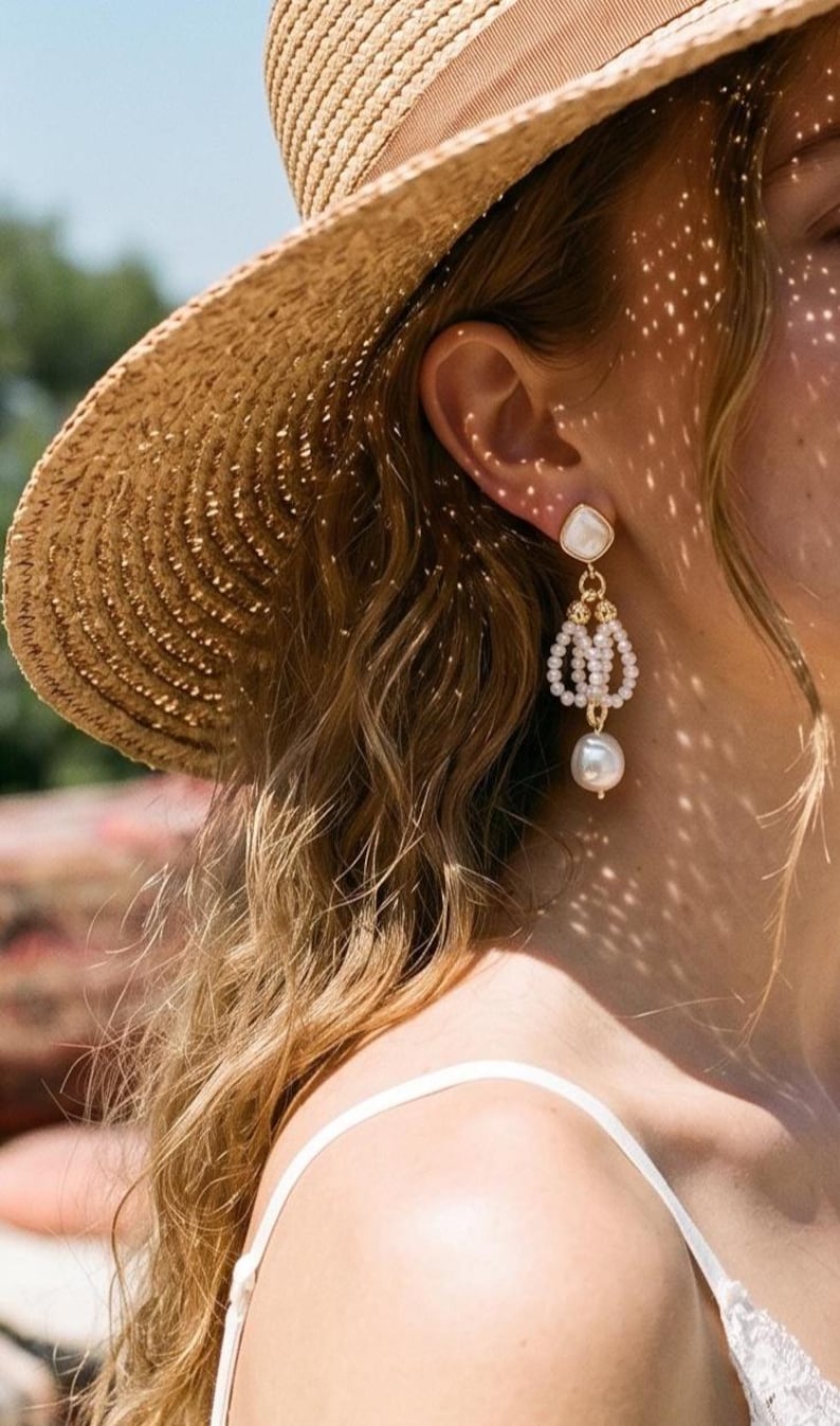 May include: A gold-tone drop earring featuring a teardrop-shaped white stone stud, a central cluster of small white seed pearls arranged in a cage-like structure, and a single large, round, off-white baroque pearl dangling at the very bottom.