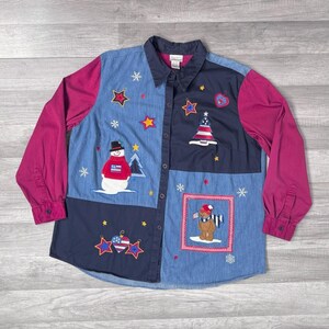 May include: A button-down shirt with a patchwork design featuring a snowman, stars, and a bear wearing a scarf. The shirt has long sleeves in a magenta color, and the body is a mix of blue denim and navy blue fabric.