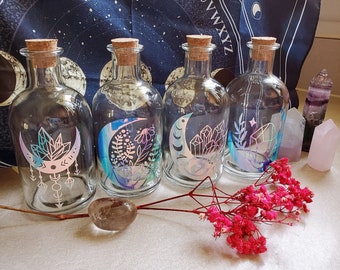 May include: Four clear glass bottles with cork stoppers and iridescent moon and crystal designs. The bottles are arranged in a row on a white surface with pink flowers and crystals.