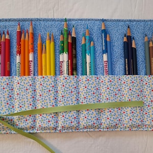 May include: A blue fabric pencil roll with a floral pattern and green ribbon. The roll is filled with colored pencils, including Crayola and Erasable brands.