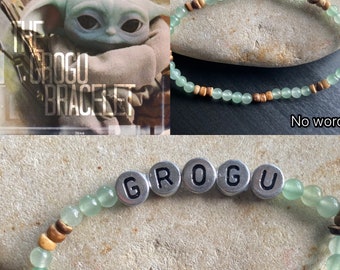 May include: A green and brown beaded bracelet with silver letter beads spelling out "GROGU".